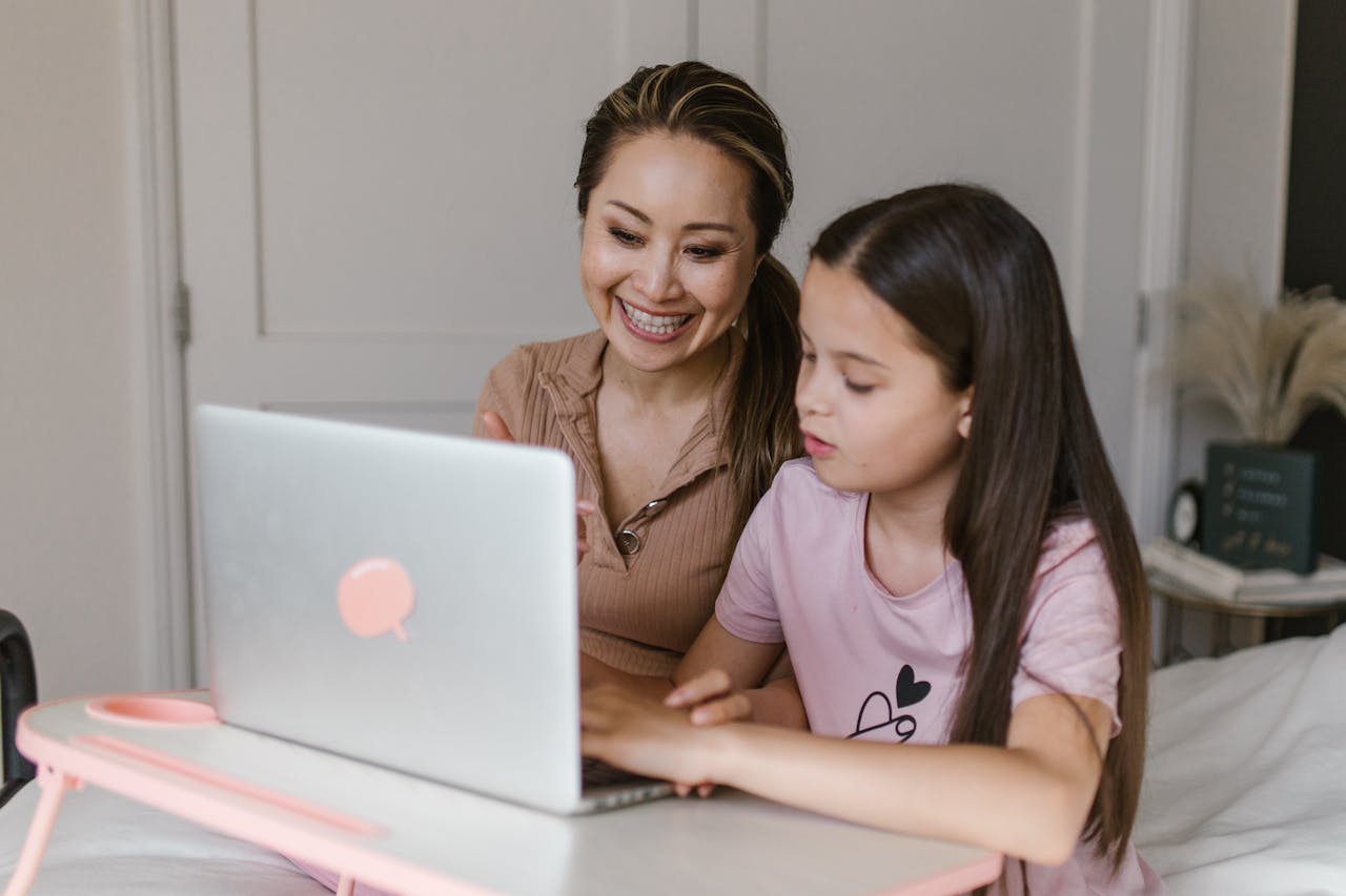 A mother and daughter smile and learn together using a laptop at home.